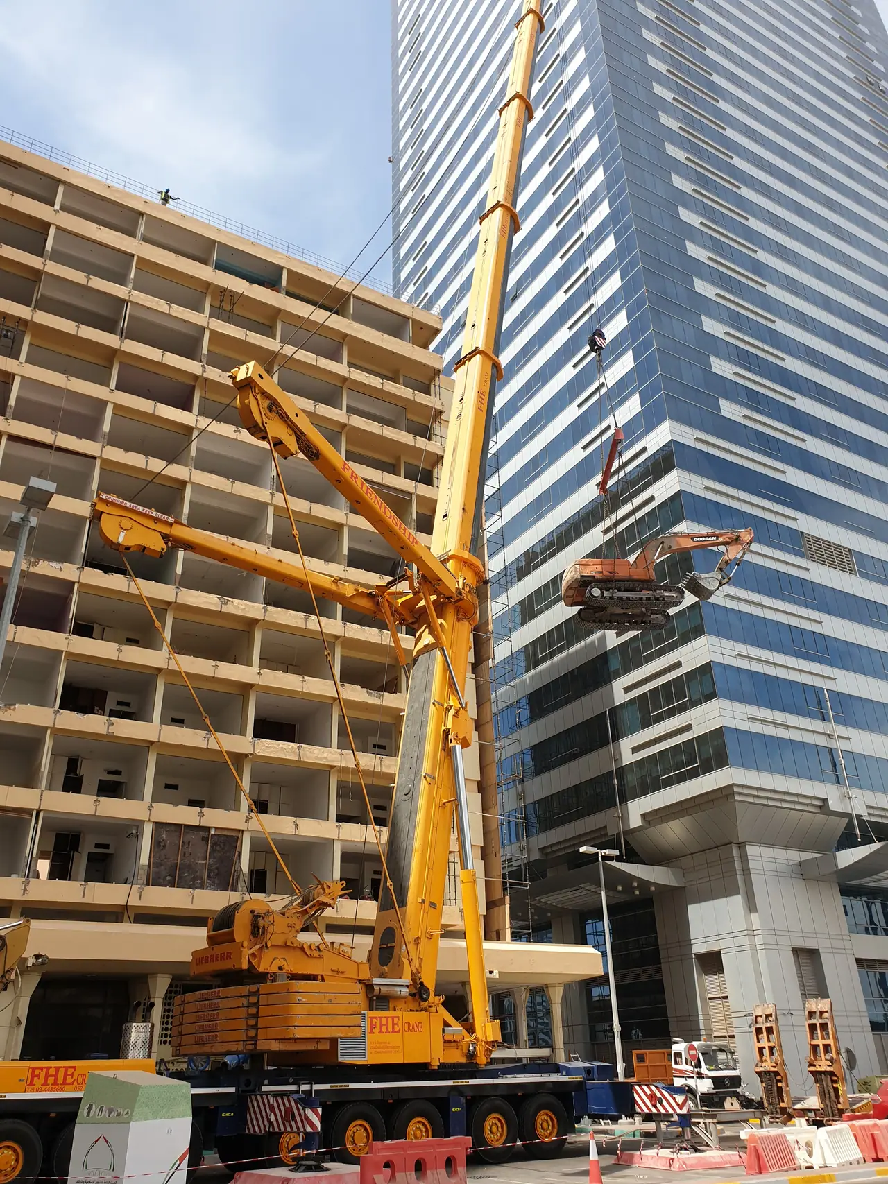 FHE crane with an excavator on the hook beside a high-rise