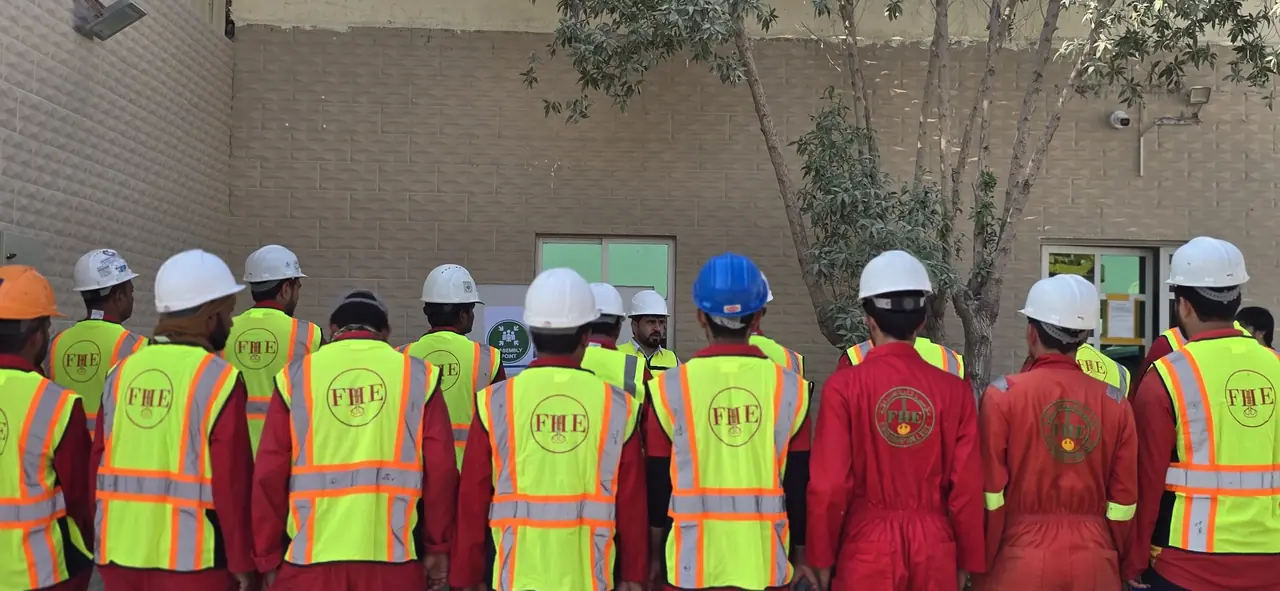 Rows of FHS crew from behind, FHE logos on their hi-vis vests and coveralls