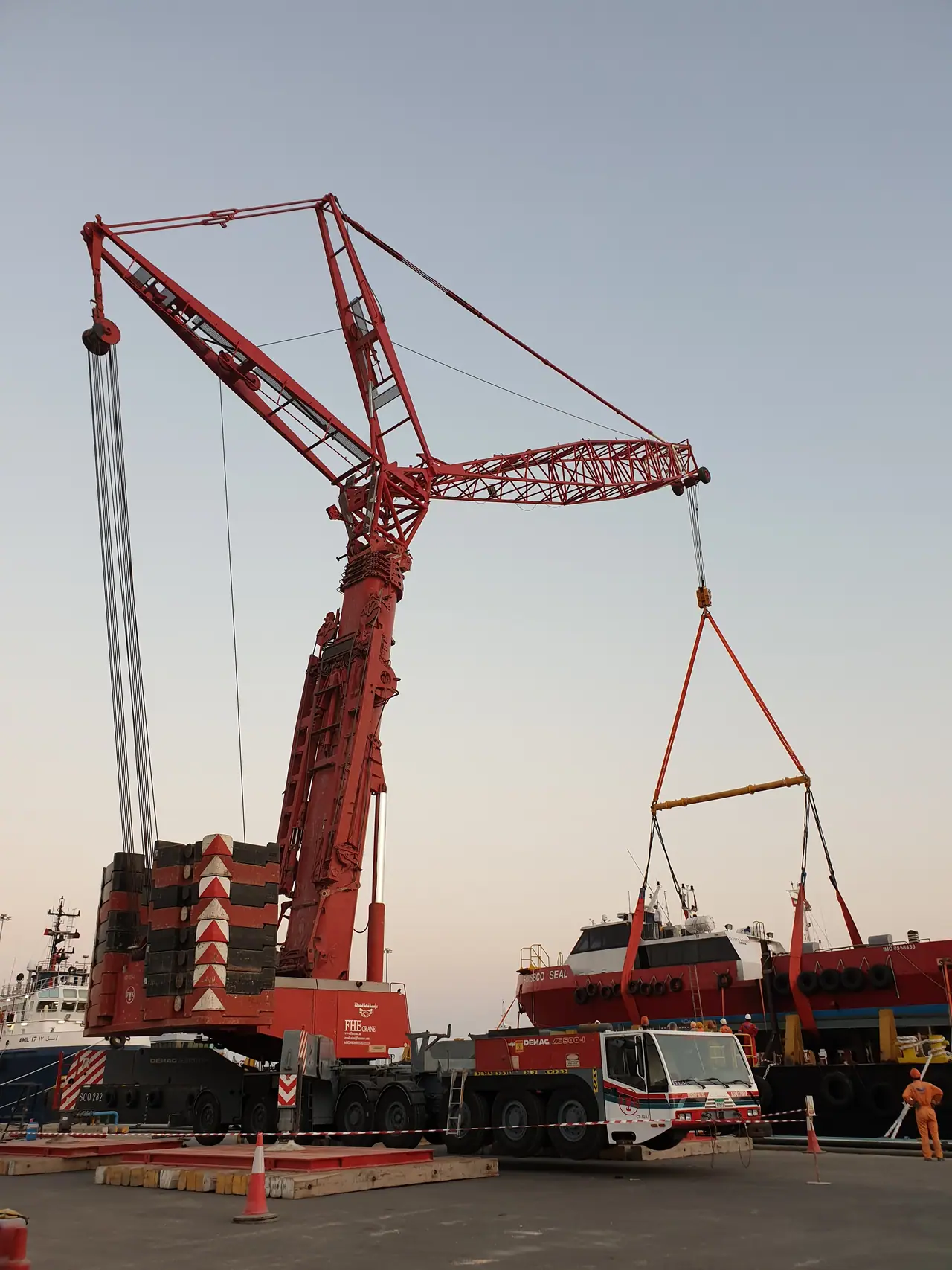 Red FHE luffing-jib crane rigged to a workboat on the quay, at dusk