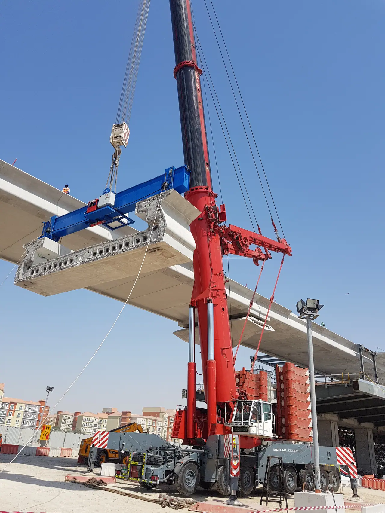 Red Demag crane with a precast bridge segment on a blue spreader beam