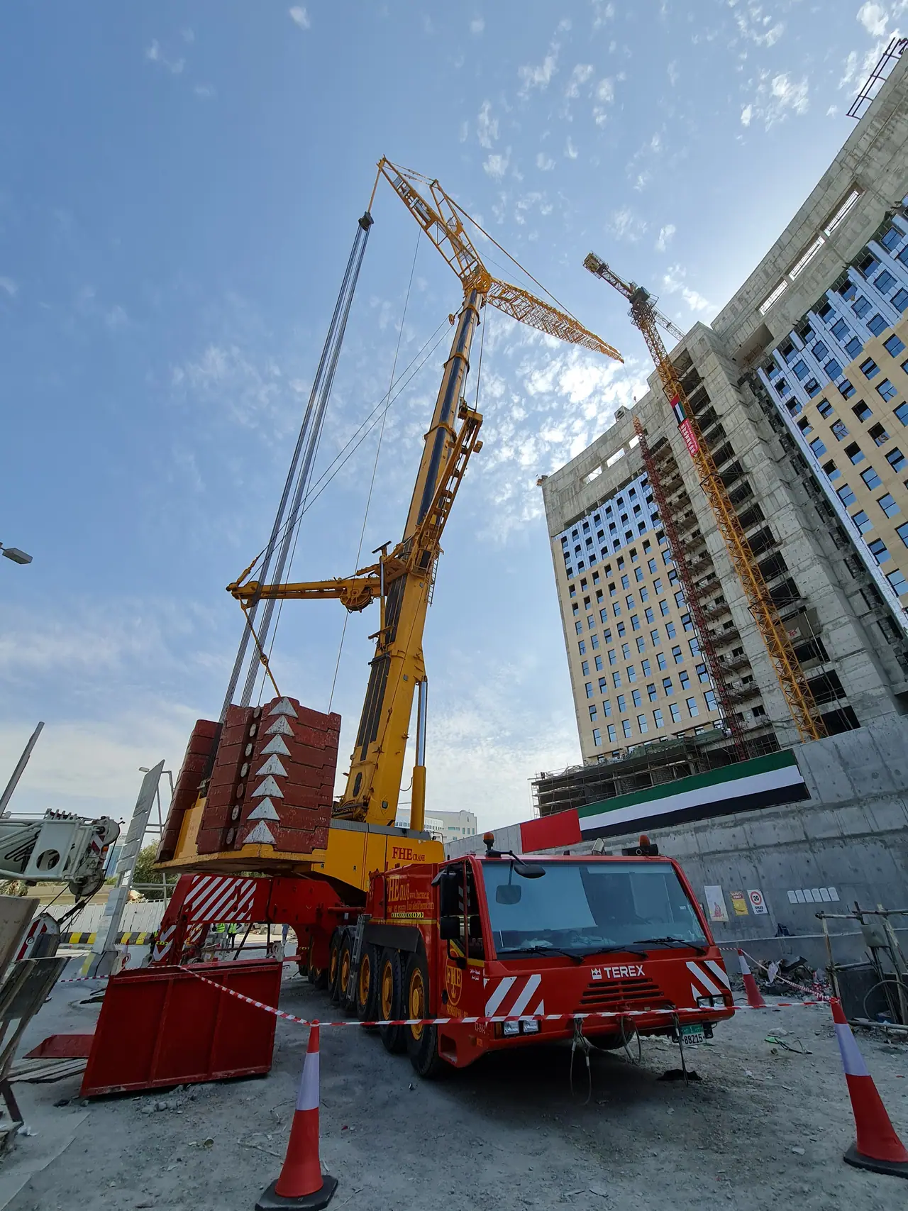 Heavy crane with a luffing jib beside a building draped with the UAE flag