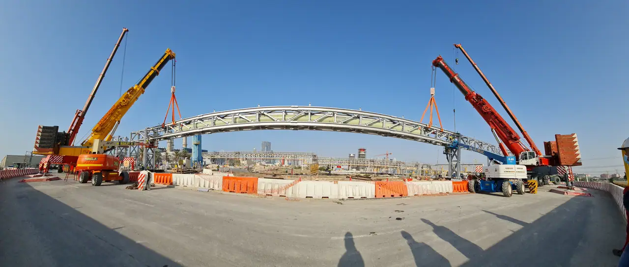 Two cranes lifting a long steel pipeline truss in tandem
