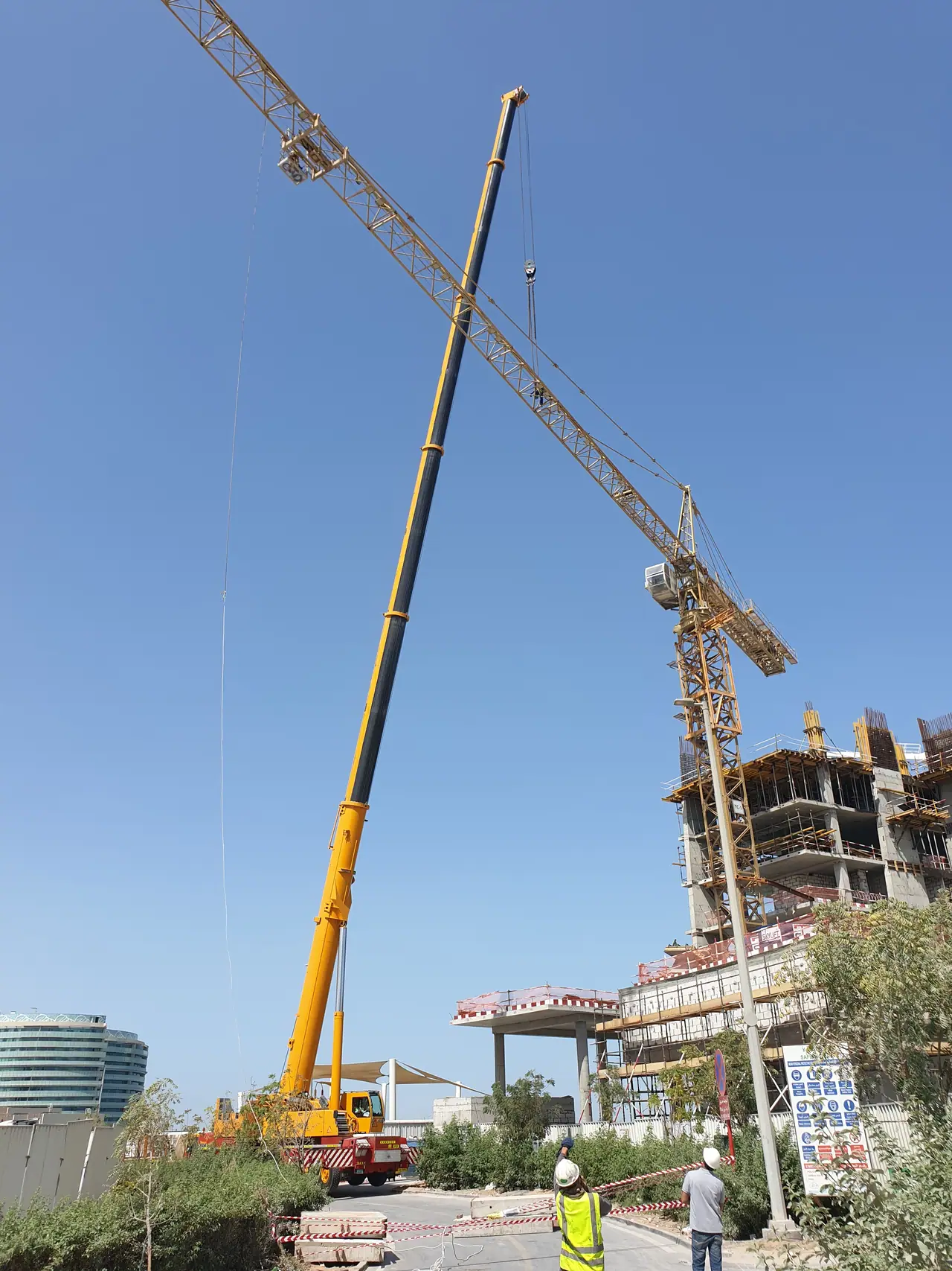 Yellow telescopic mobile crane working at a tower crane on a city site