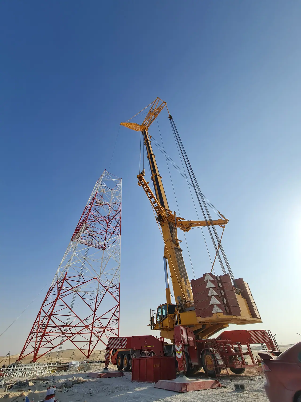 Heavy crane rigged beside a red-and-white lattice transmission tower